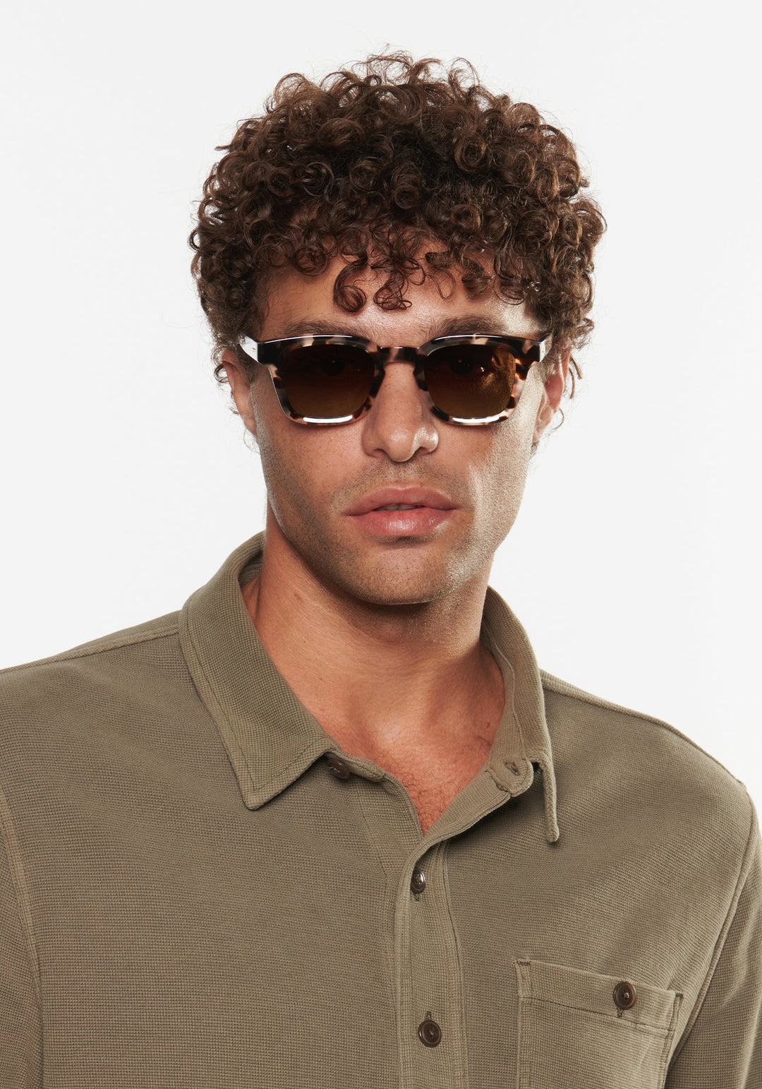 Man wearing sunglasses and a green polo shirt against a white background