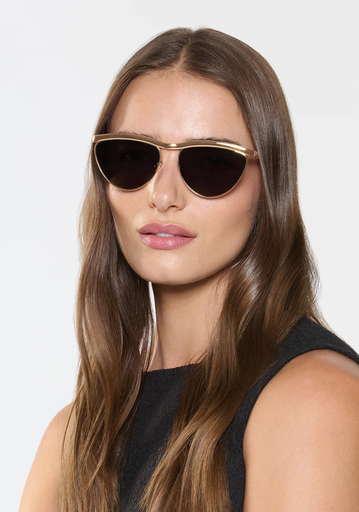 Woman wearing gold-framed sunglasses against a white background