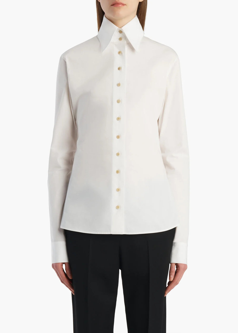 A model wearing a white long-sleeve button-down shirt with a pointed collar and black trousers, shown from the neck down against a plain white background.
