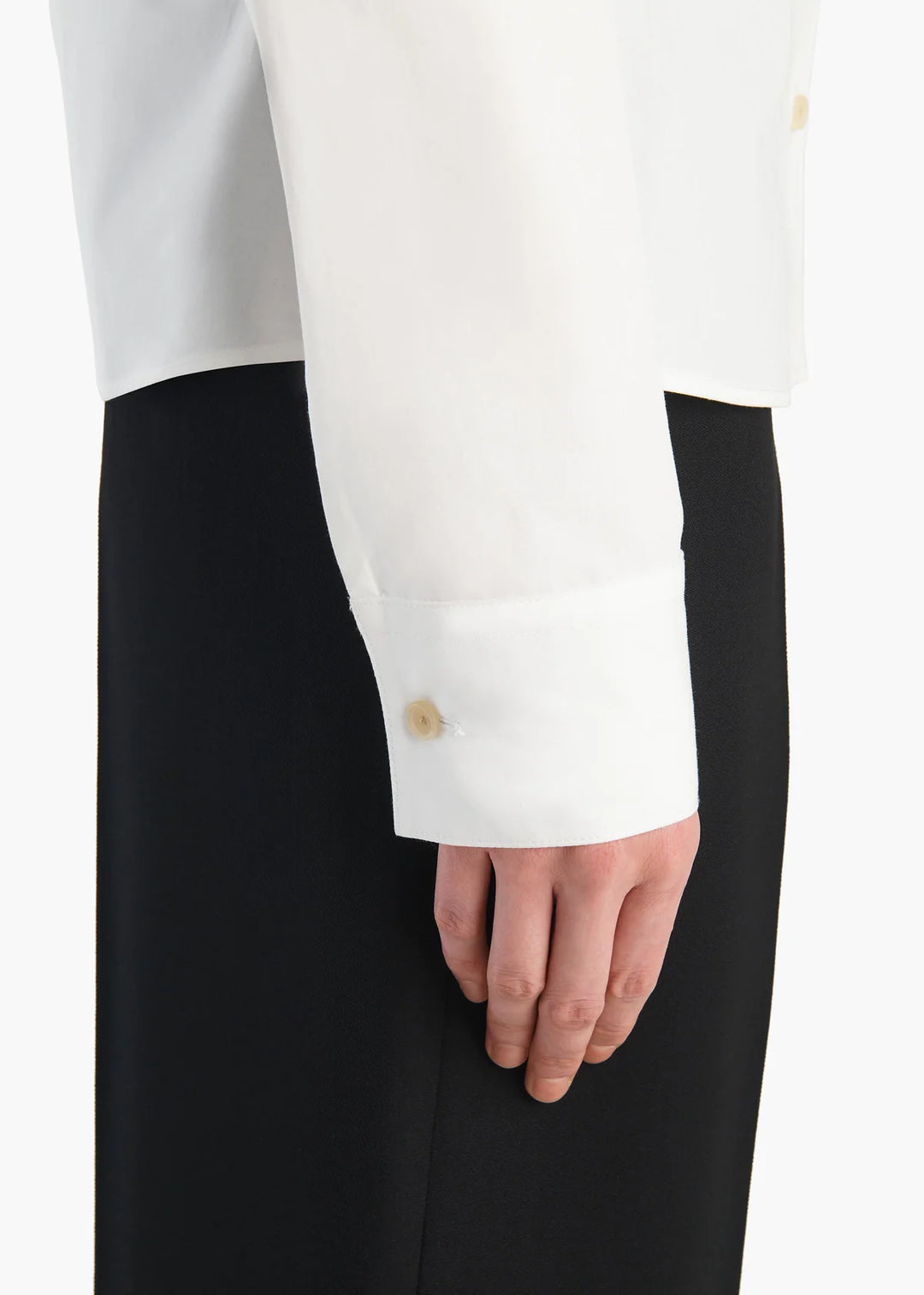 Close-up of a white shirt with black pants and a gold button on a white background