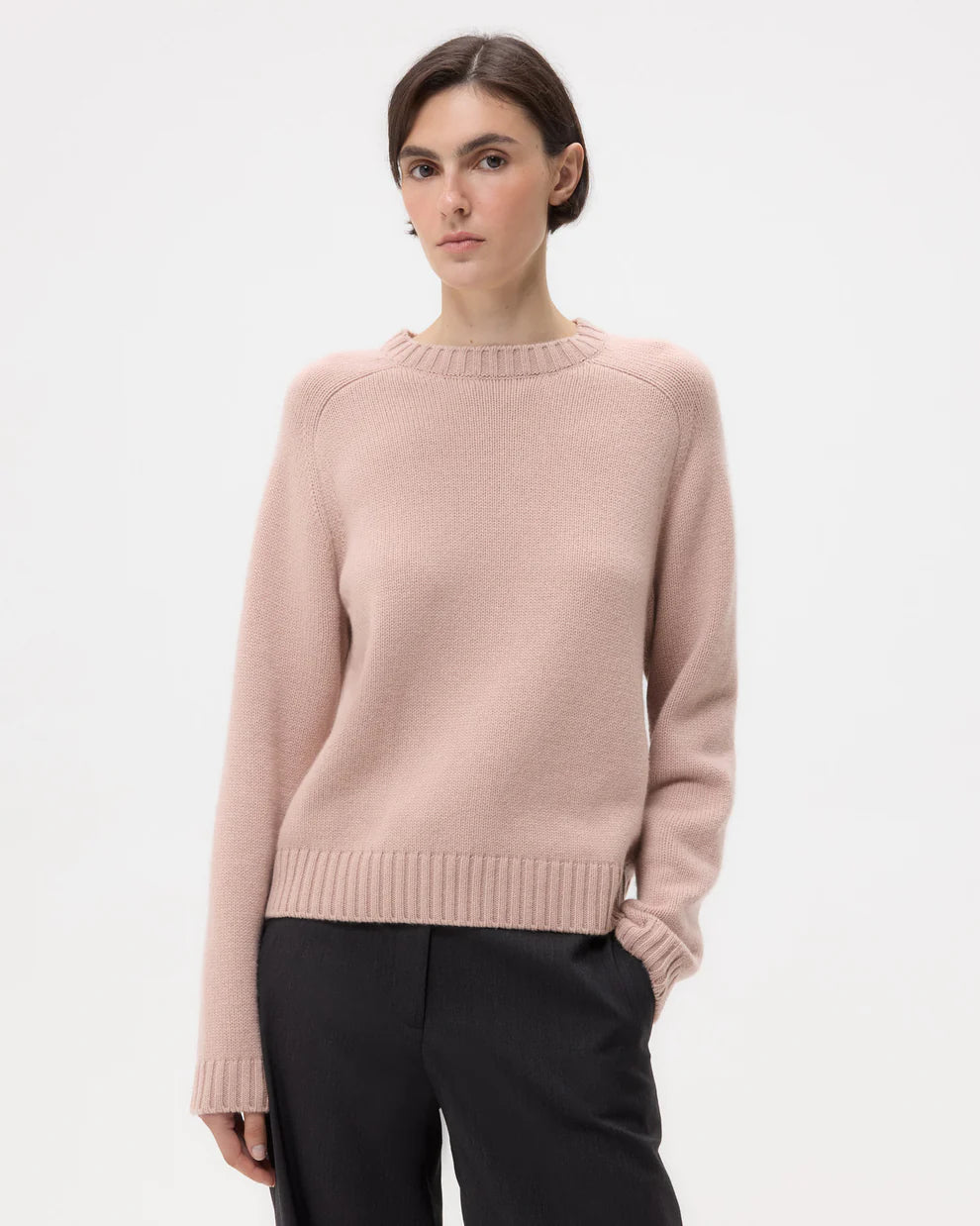Woman wearing a light pink sweater and black pants on a white background