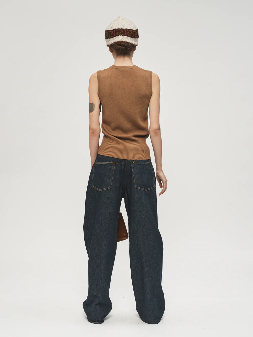 Person wearing a brown sleeveless sweater and dark blue jeans on a white background