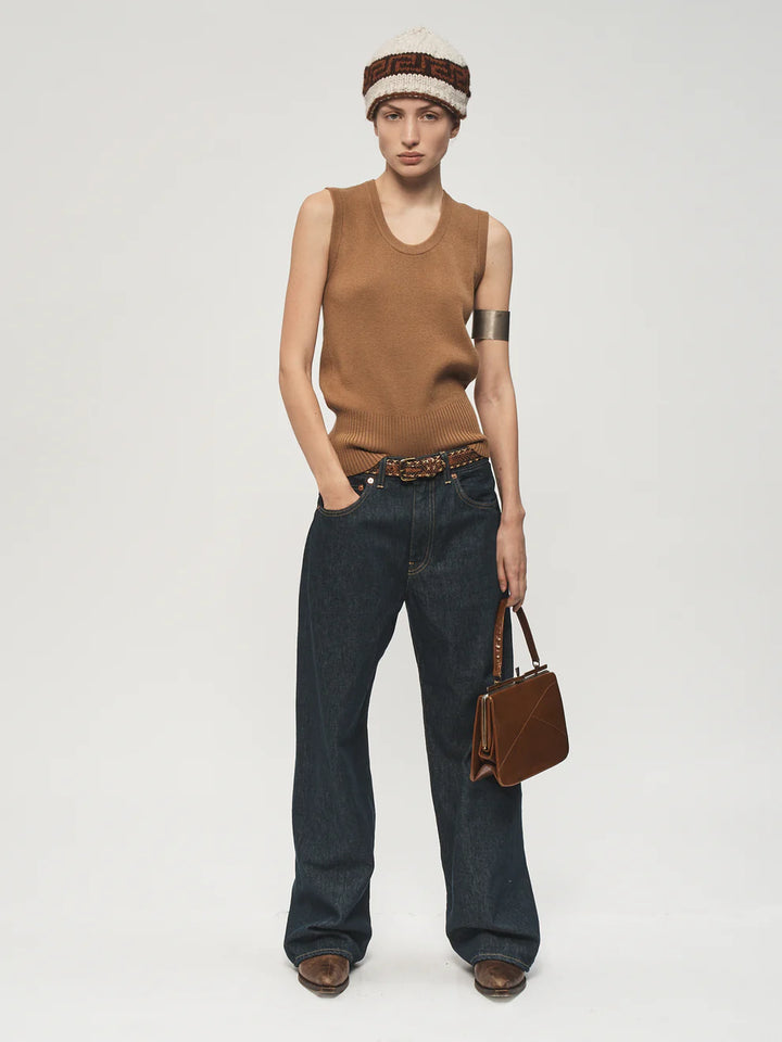 Person wearing a brown sleeveless top, dark jeans, and a brown hat on a white background