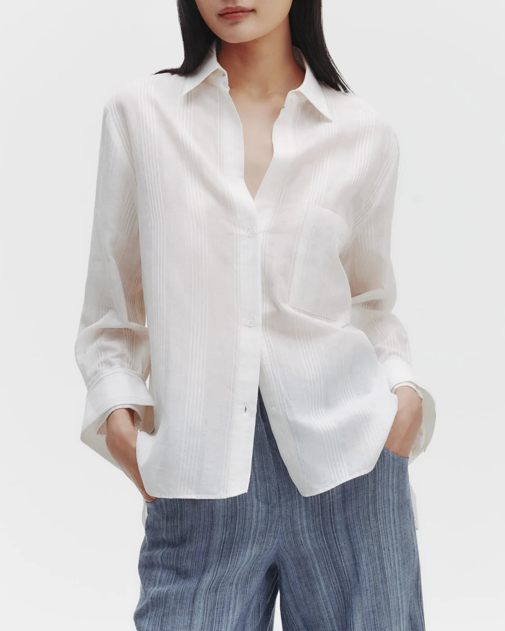 A woman wearing a white oversized button-down shirt with a striped pattern and a spread collar.