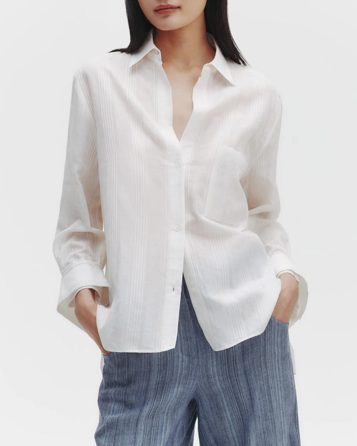 A woman wearing a white oversized button-down shirt with a striped pattern and a spread collar.