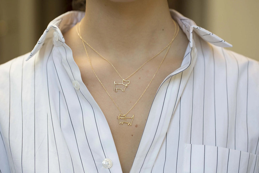 Person wearing two gold necklaces with dog pendants on a white shirt.
