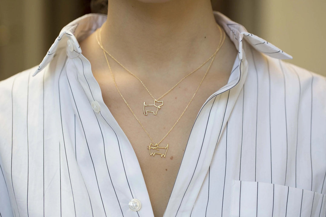 Person wearing two gold necklaces with dog pendants on a white shirt.