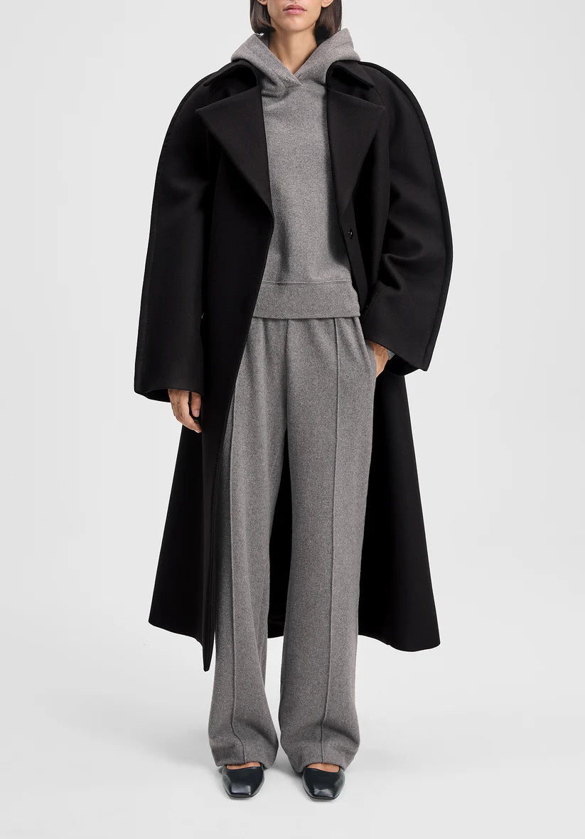 Person wearing a black coat over a gray outfit on a white background