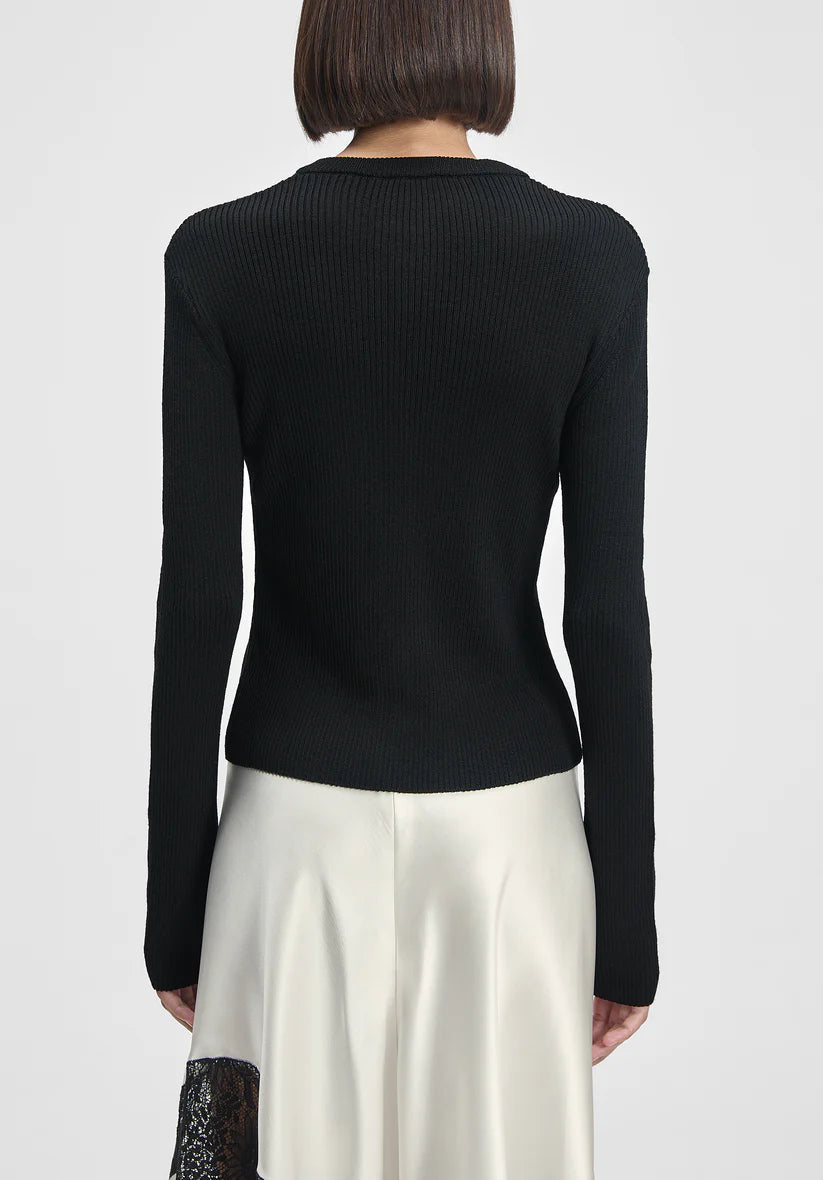 Person wearing a black long-sleeve top and white pants on a plain background