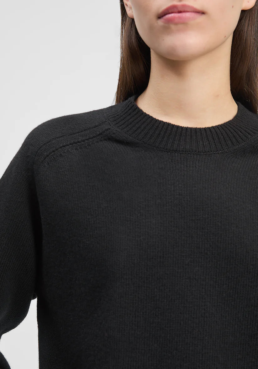 Black sweater worn by a person on a light gray background