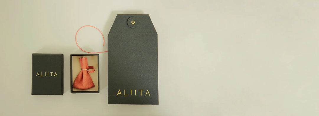 Black 'ALIITA' branded box with a pink bow on a beige background