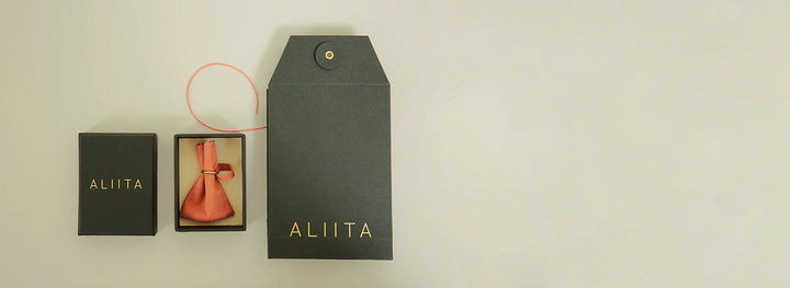 Black 'ALIITA' branded box with a pink bow on a beige background