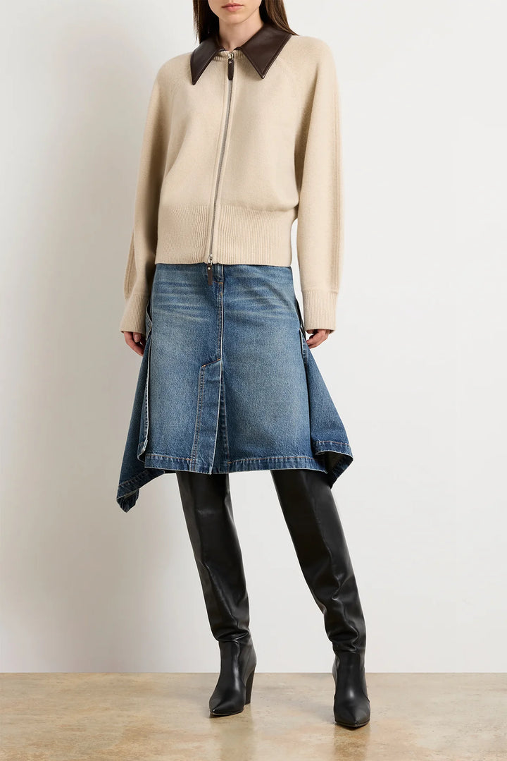 Person wearing a beige jacket with a brown collar, blue denim skirt, and black leather boots on a plain background.