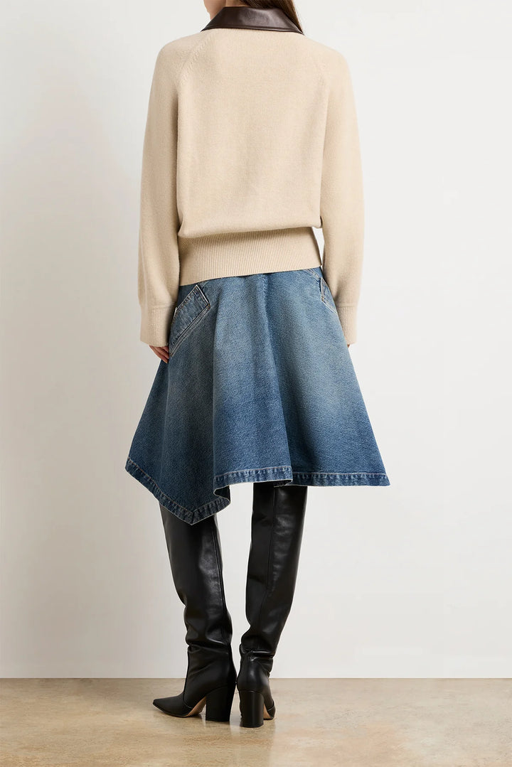 Person wearing a beige sweater, blue denim skirt, and black knee-high boots on a plain background