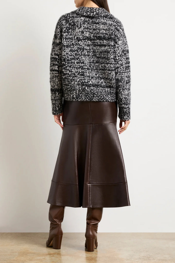 Person wearing a black and white patterned sweater with a brown leather skirt on a plain background