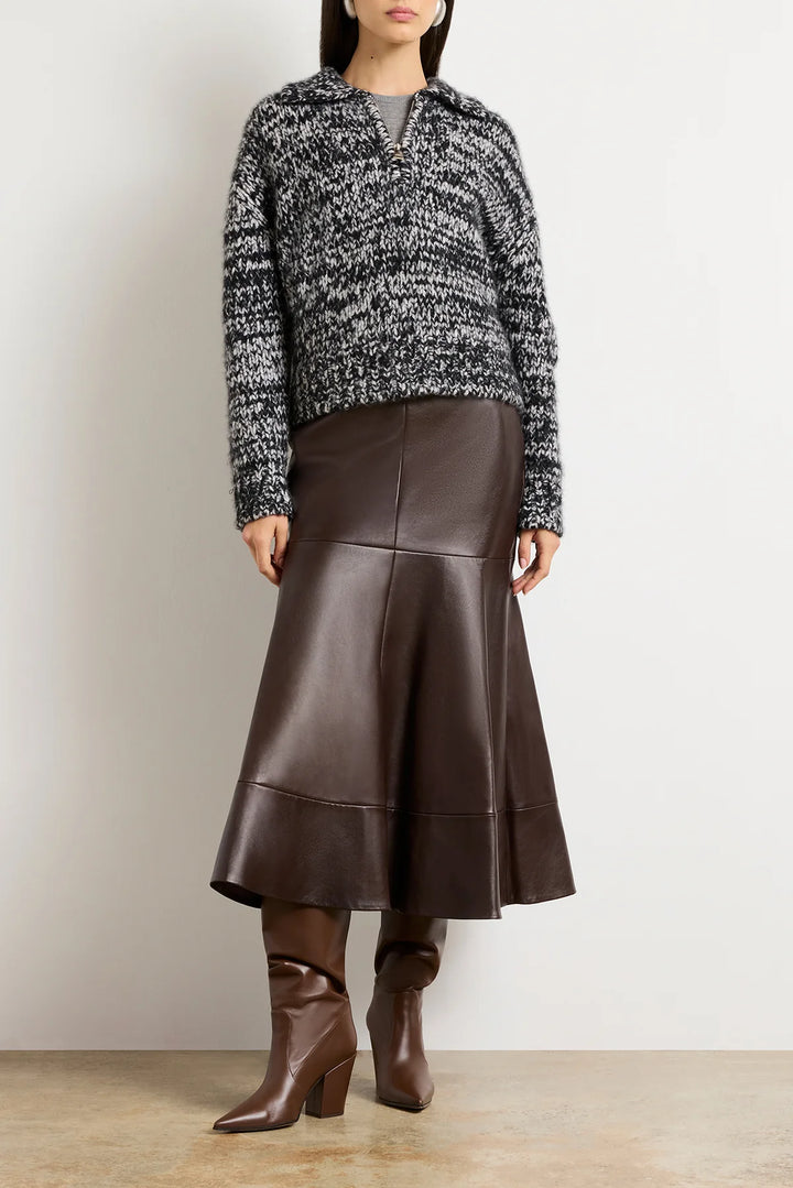 Woman wearing a patterned sweater and brown leather skirt with boots on a plain background