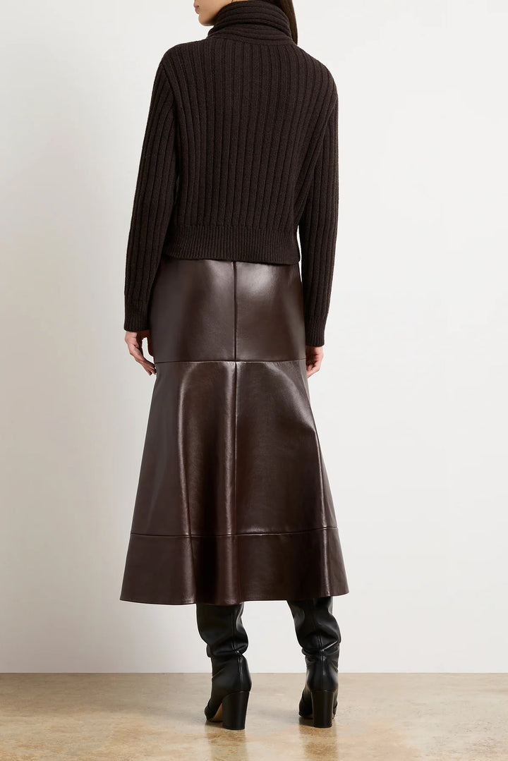 Person wearing a brown turtleneck sweater and leather skirt on a plain background