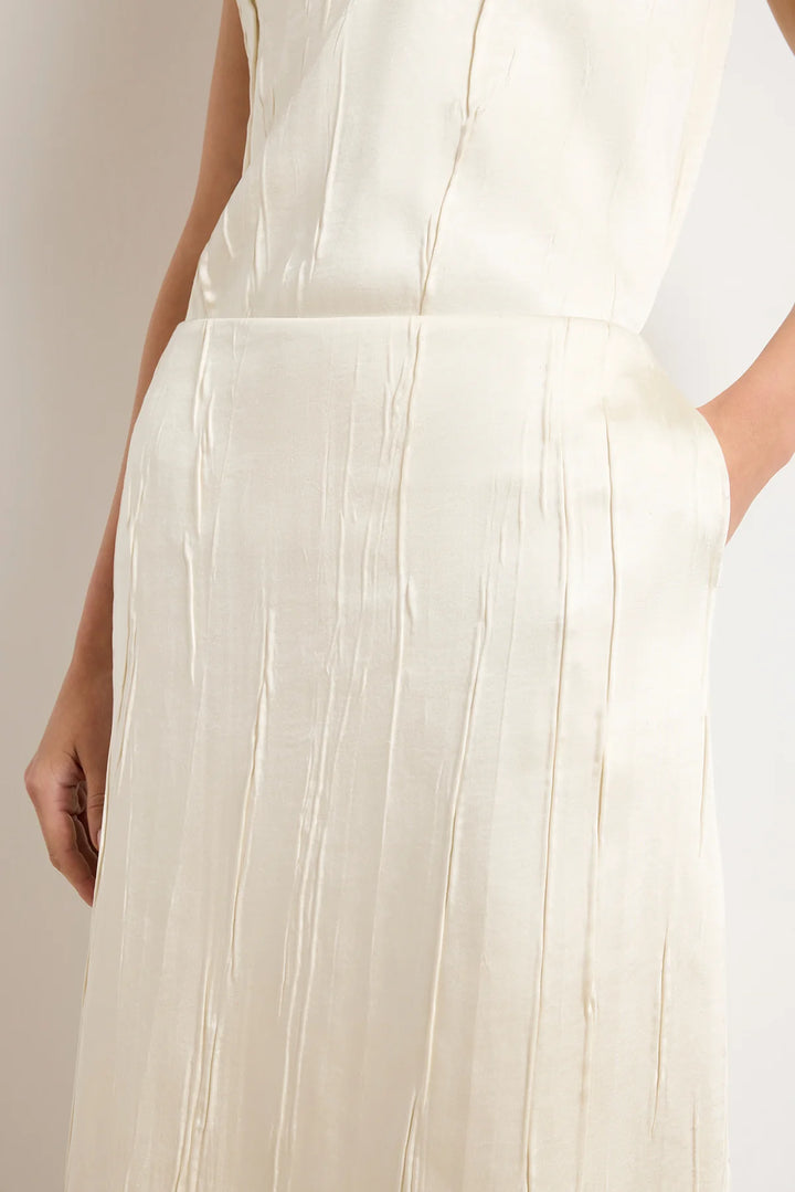 Close-up of a person wearing a white dress with pleated details on a plain background