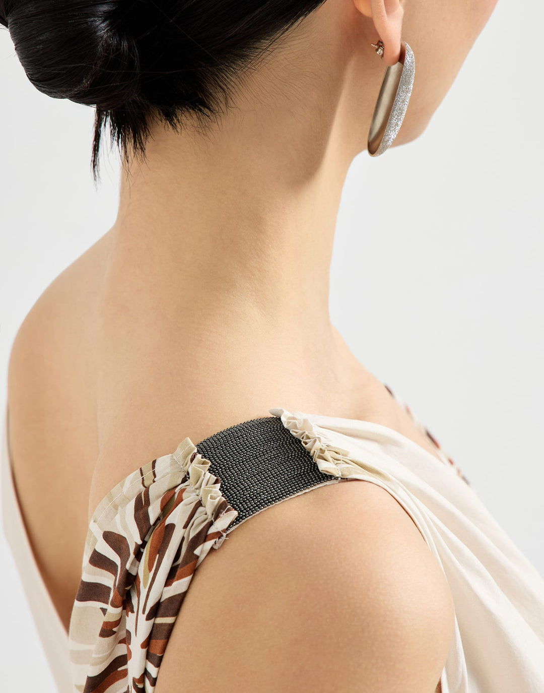 Close-up of a person wearing hoop earrings with a neutral background