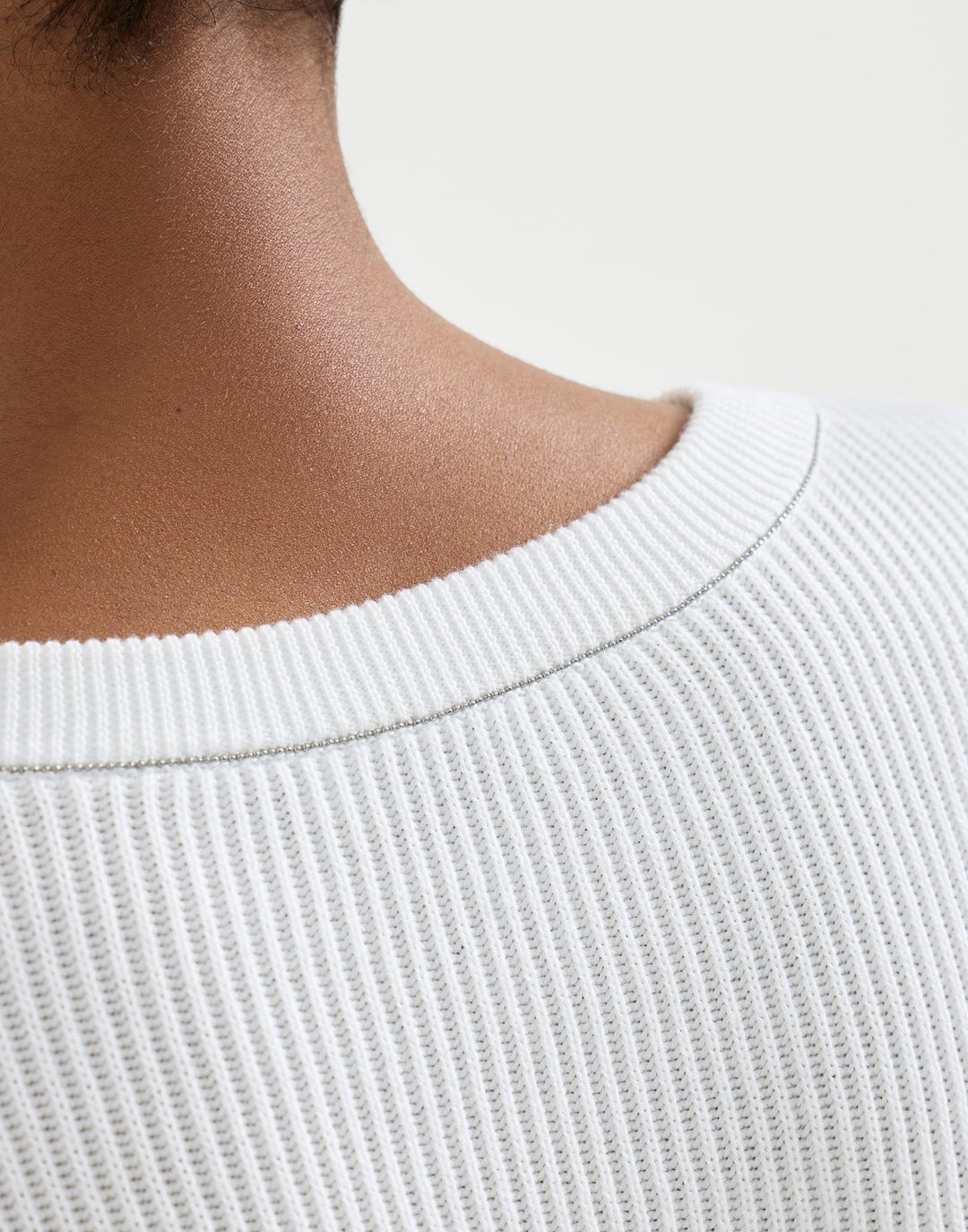 Close-up of a person wearing a white ribbed sweater on a light background