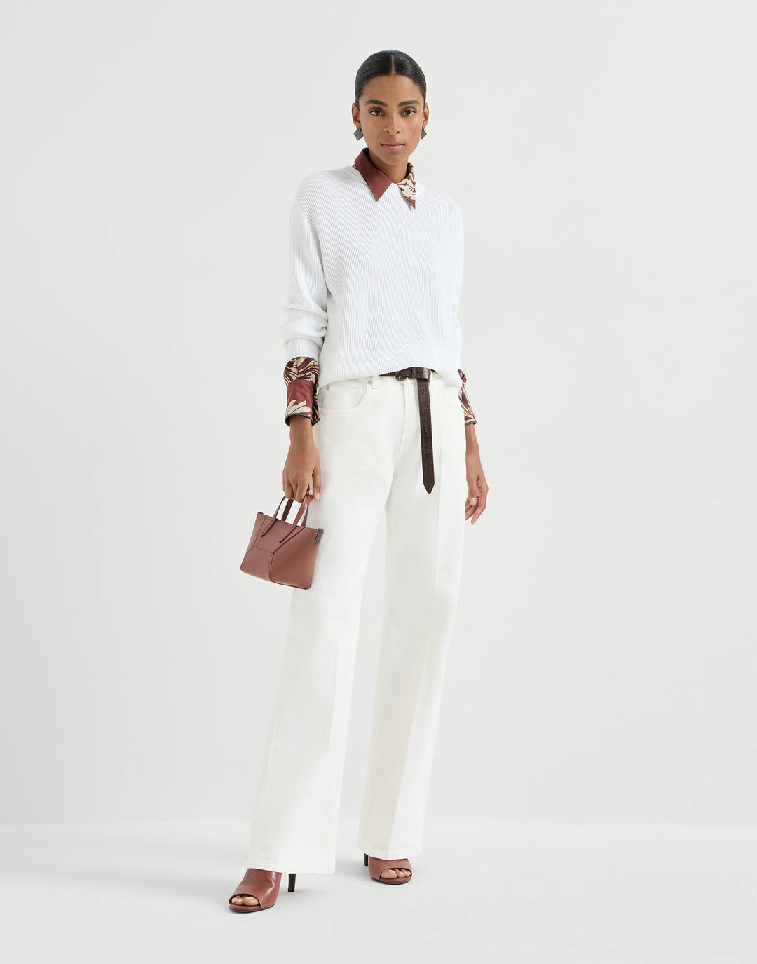 Woman wearing a white outfit with a brown belt and carrying a pink handbag on a light gray background