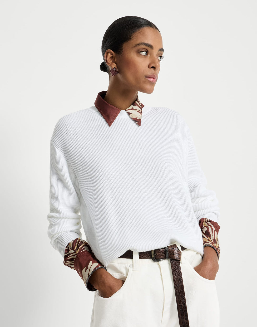 Woman wearing a white sweater over a patterned shirt with a plain background
