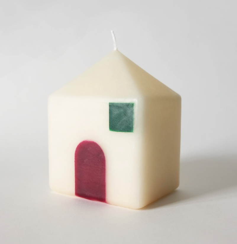 Candle shaped like a house with a red door and green window on a white background