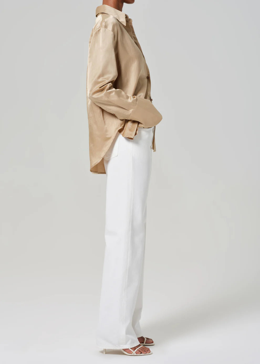 Person wearing a beige shirt and white pants on a plain background