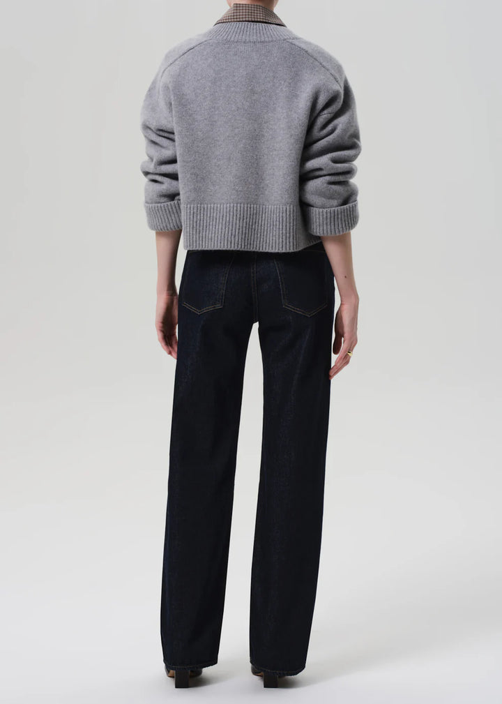 Person wearing a gray sweater and black pants on a white background