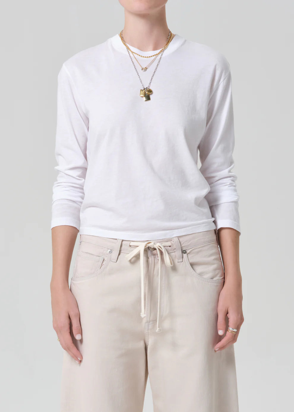 Person wearing a white long-sleeve shirt and beige pants on a plain background