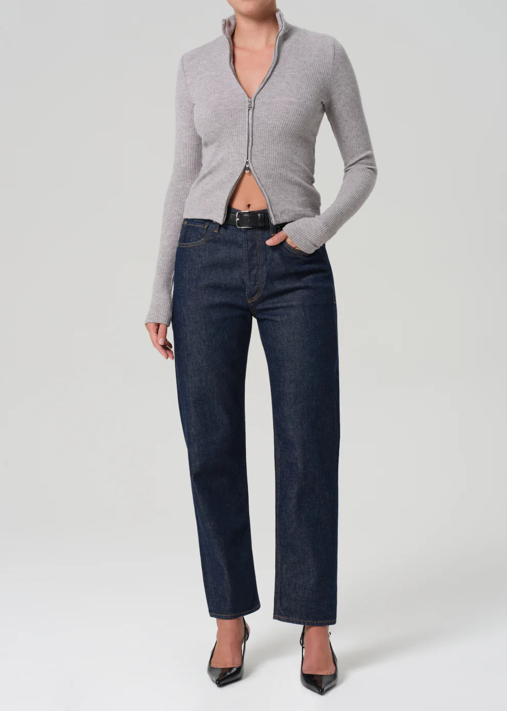 Person wearing a gray zip-up sweater and dark blue jeans on a white background