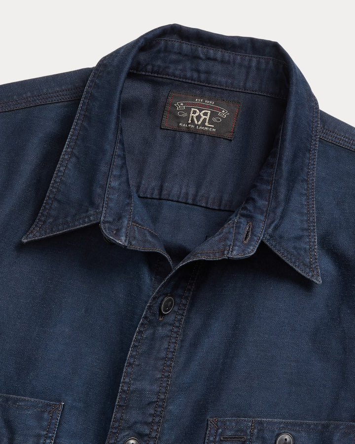 Close-up of a blue denim shirt with a brand label on a gray background