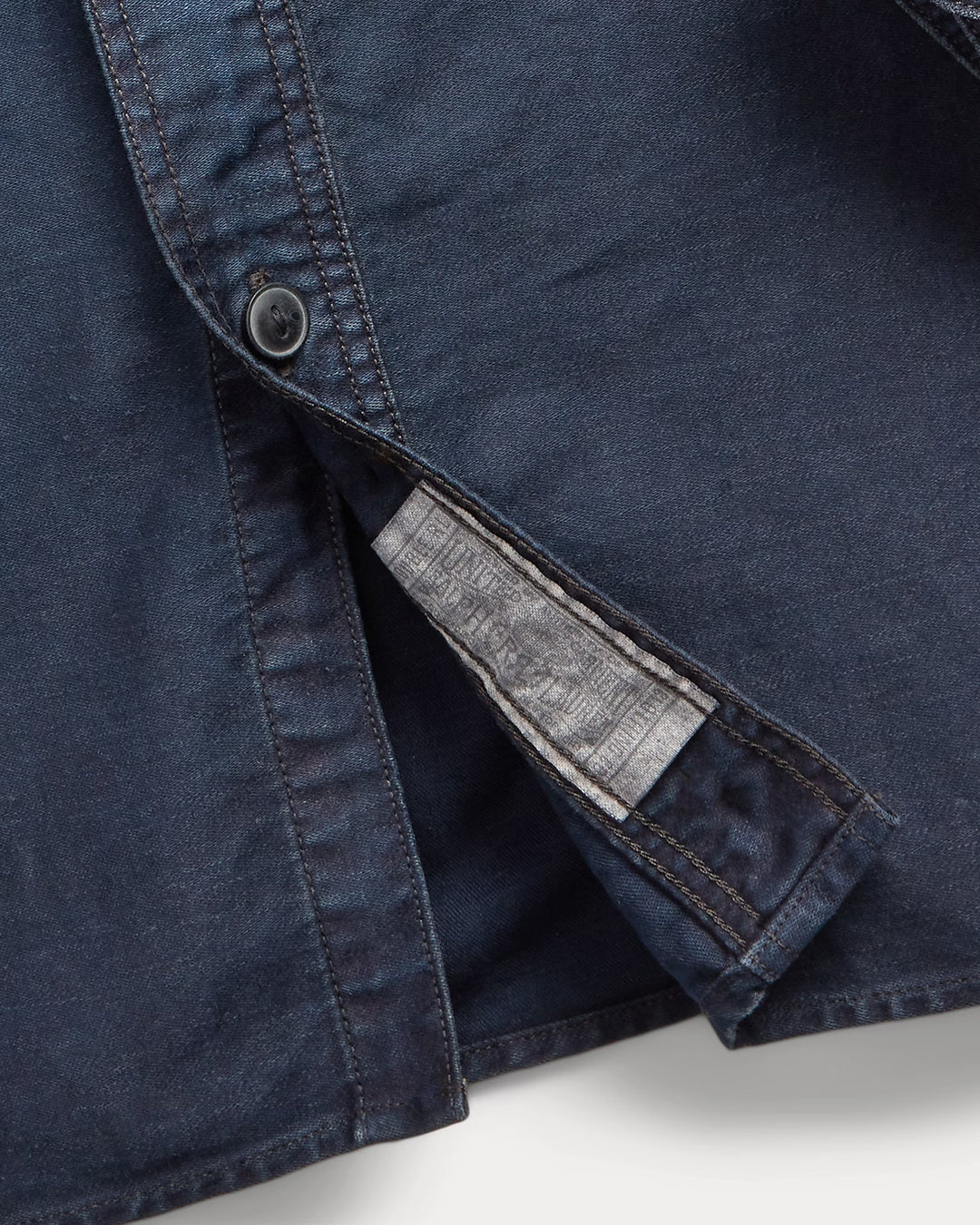 Close-up of a blue denim shirt with a button and gray lining on a white background