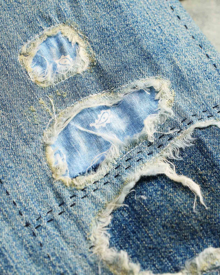 Close-up of a distressed denim fabric with frayed edges and worn-out areas.