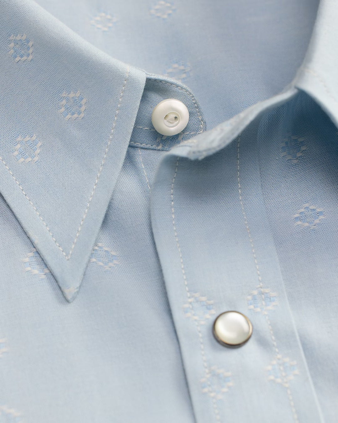 Close-up of a light blue shirt with white buttons and subtle pattern