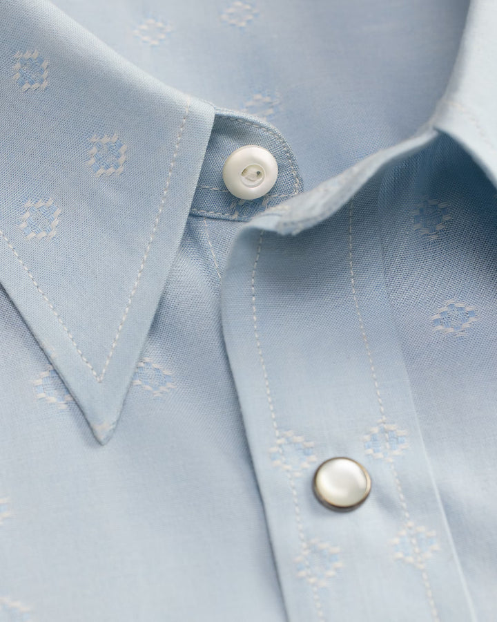 Close-up of a light blue shirt with white buttons and subtle pattern