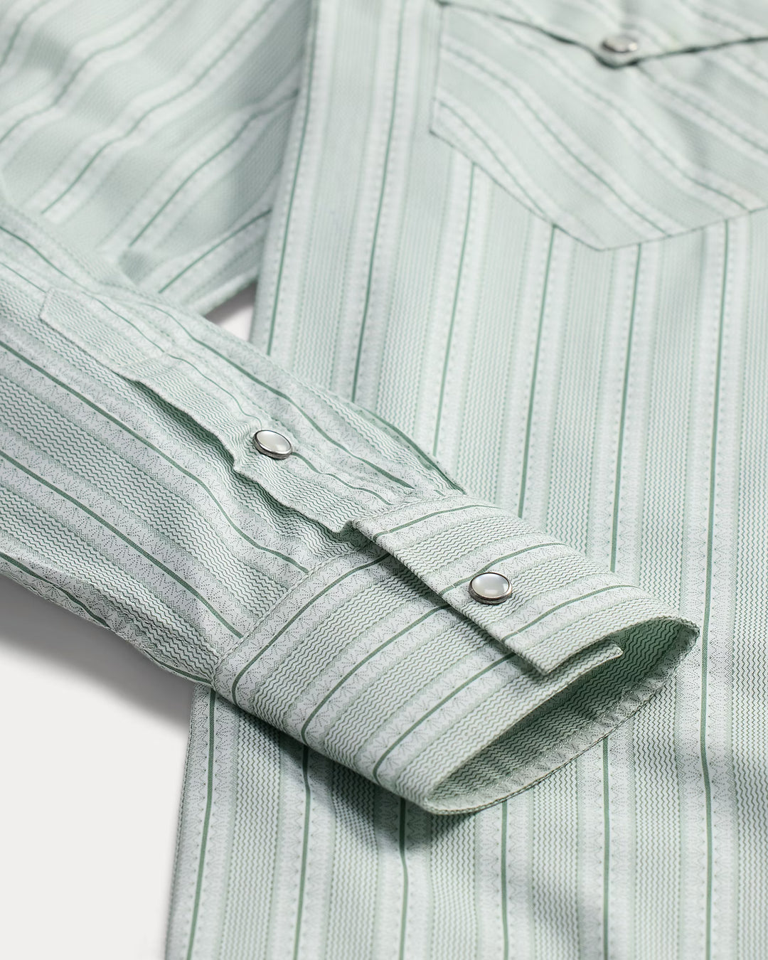 Close-up of a light green striped shirt with rolled-up sleeve on a white background