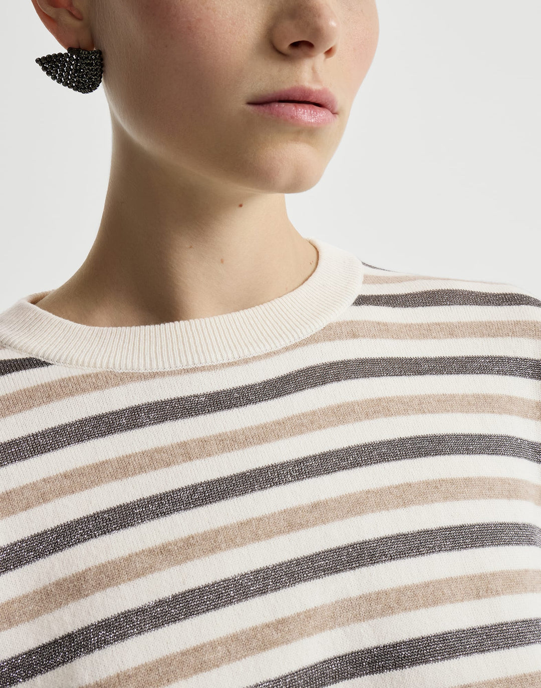 Close-up of a model wearing a cream crewneck sweater with horizontal stripes in beige and dark gray, featuring a textured black beaded earring.