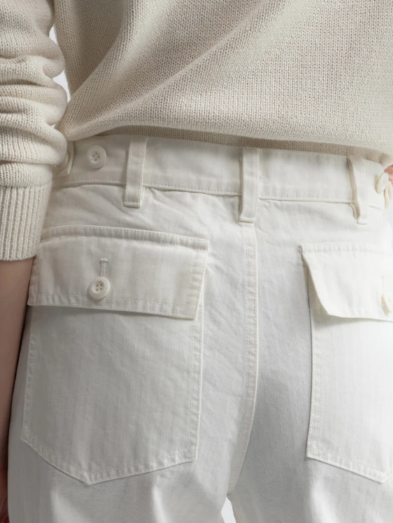 Close-up of a person wearing a beige sweater and light-colored pants with pockets.