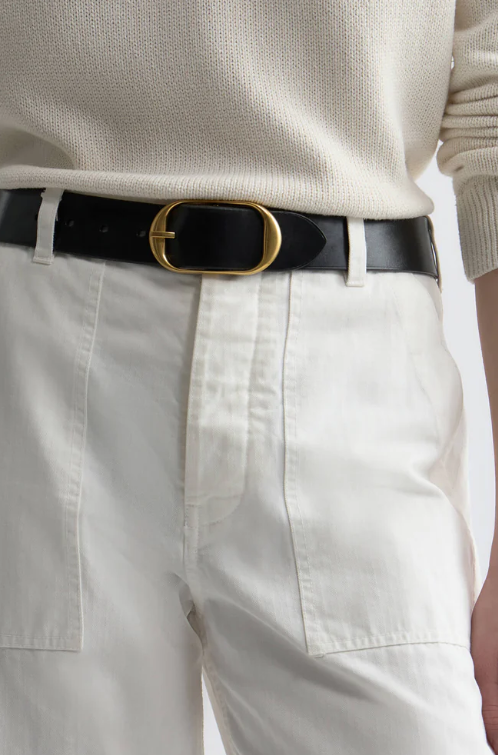 Close-up of a person wearing a black belt with a gold buckle, white pants, and a beige sweater.