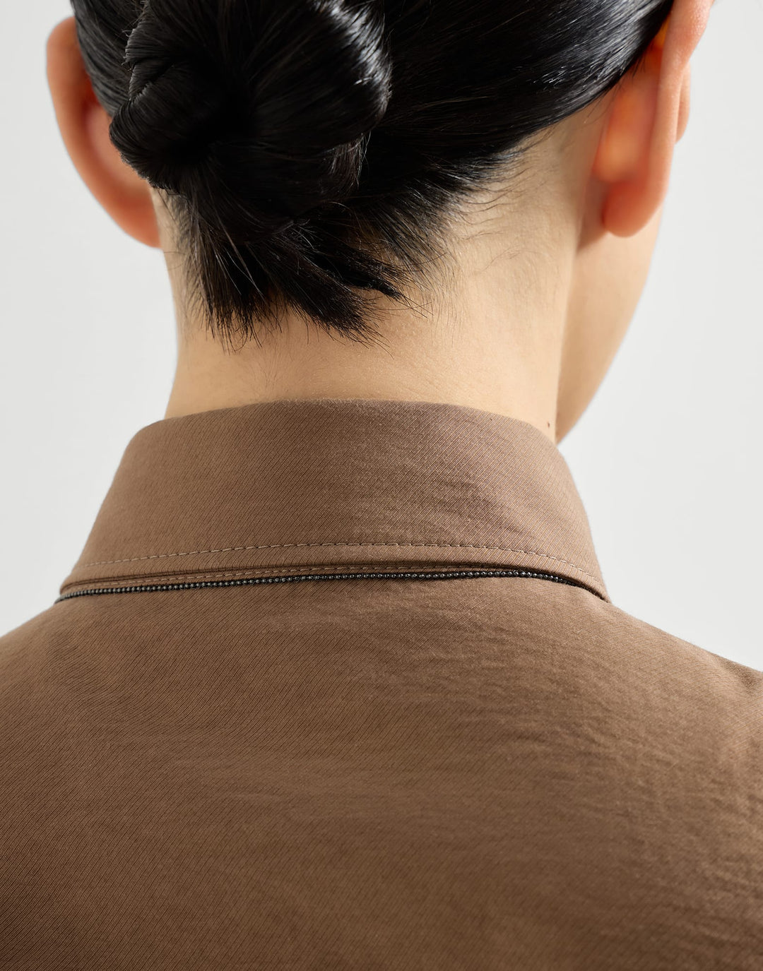 Close-up of a person wearing a brown shirt with a plain background