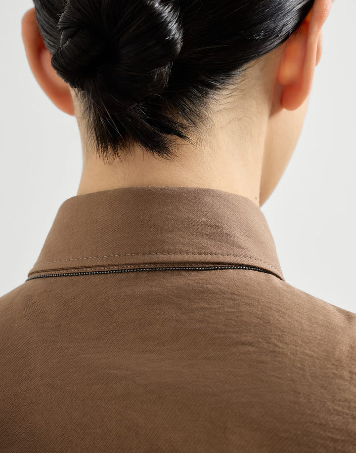 Close-up of a person wearing a brown shirt with a plain background