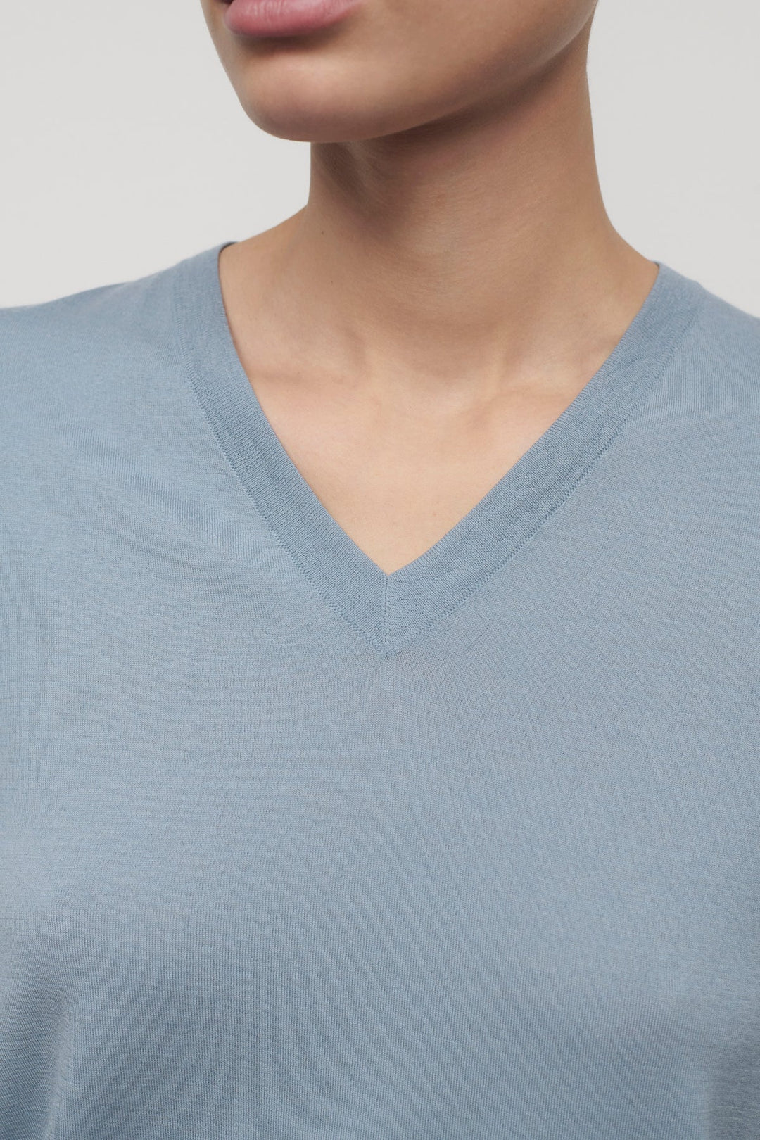 Close-up of a person wearing a light blue V-neck shirt against a neutral background