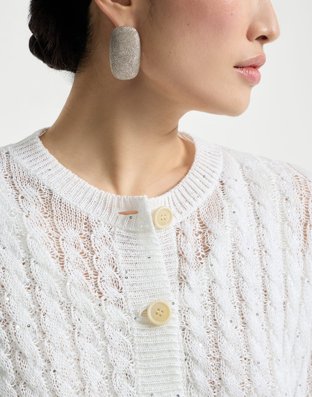 Close-up of a person wearing a white textured sweater with buttons, focusing on the collar area.