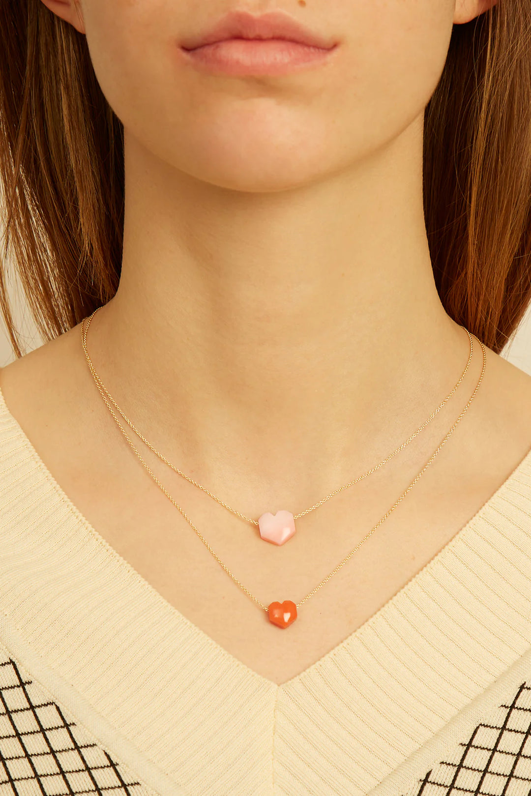 Close-up of a person wearing two delicate necklaces with heart-shaped pendants.