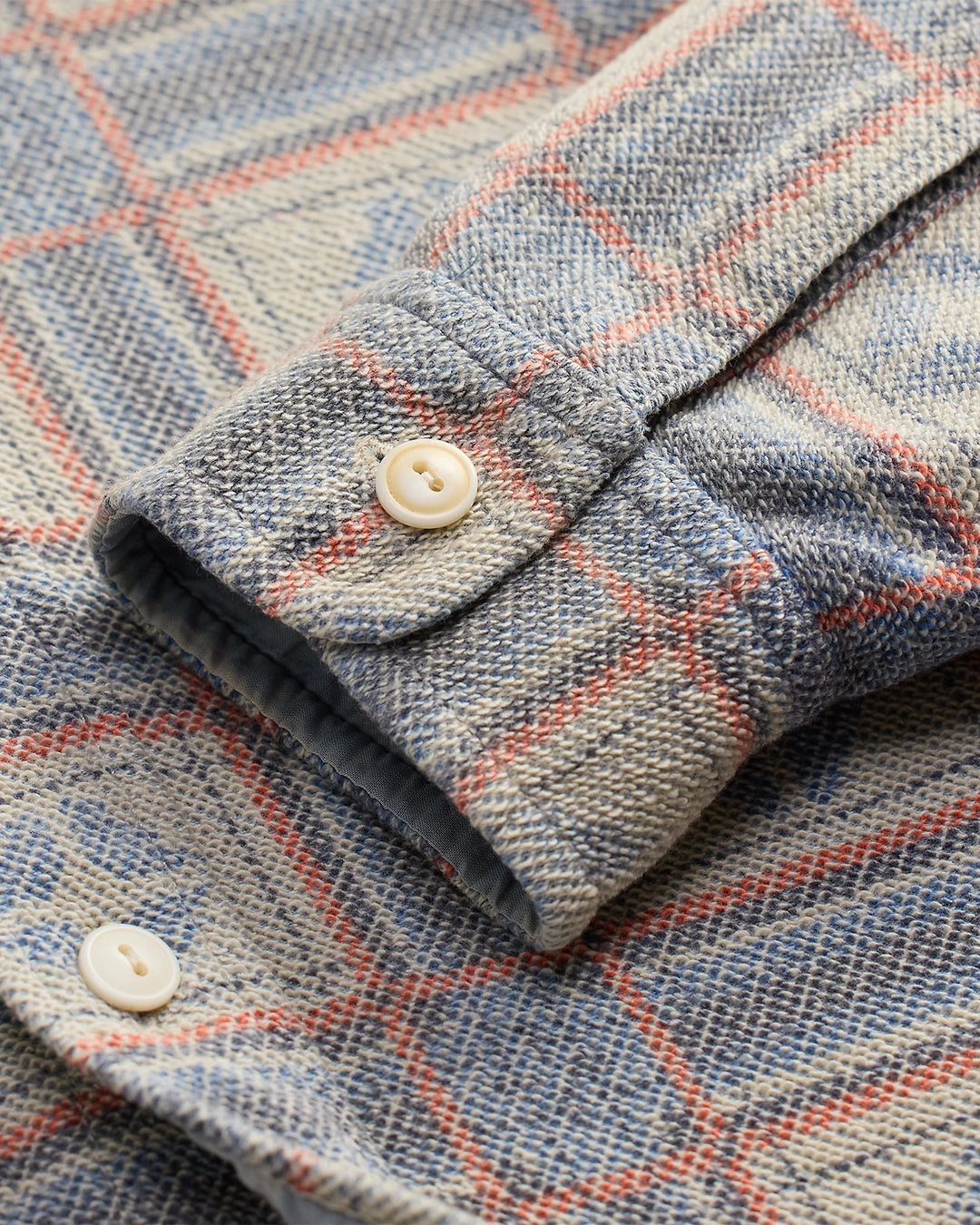 Close-up of a plaid fabric with a button, featuring blue, red, and beige colors.
