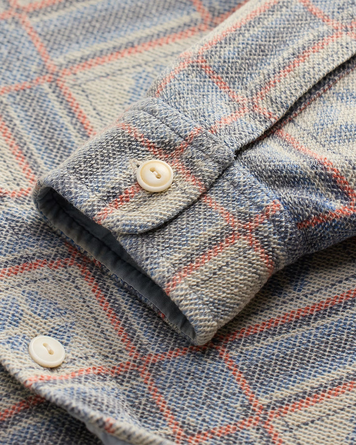 Close-up of a plaid fabric with a button, featuring blue, red, and beige colors.
