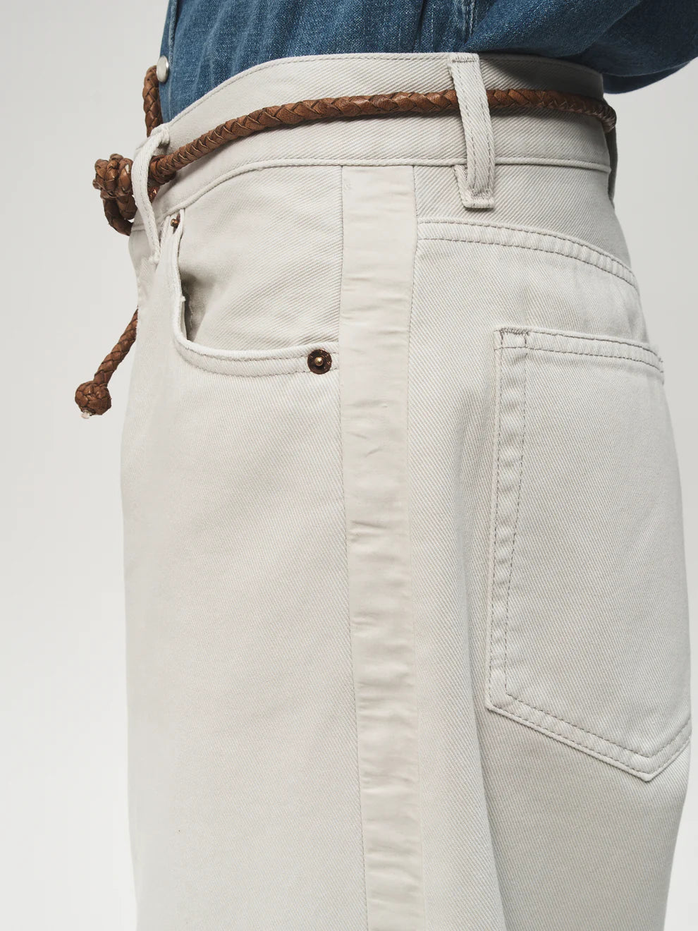 Close-up of light-colored jeans with a brown belt on a white background