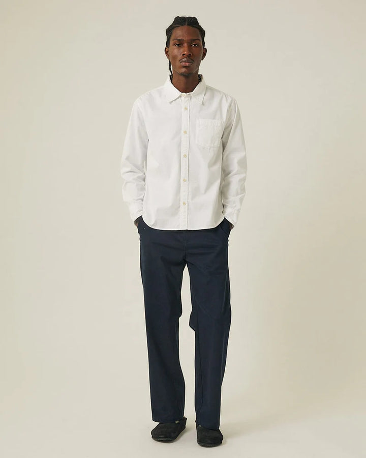 Man wearing a white shirt and navy pants on a plain background