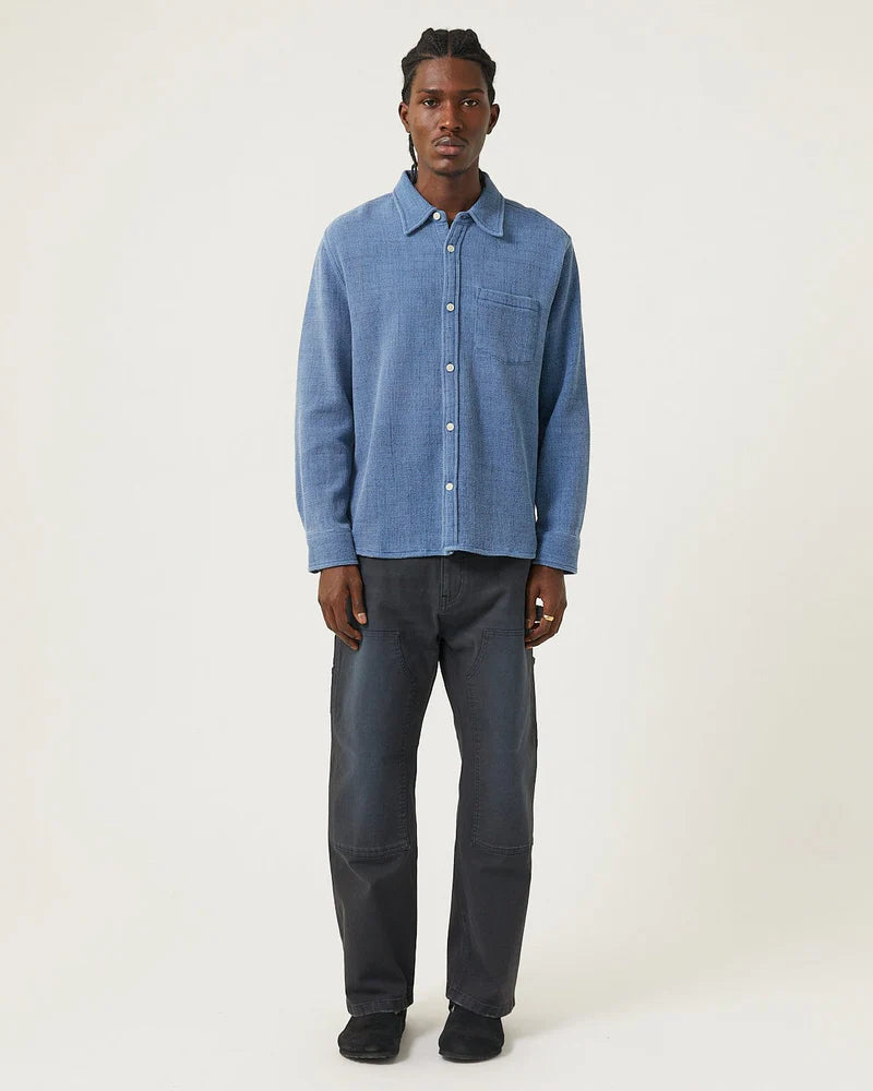 Man wearing a blue shirt and dark pants on a white background